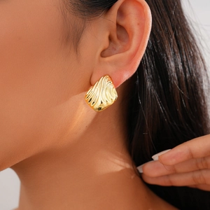 Close-up of golden metal earrings with irregular textured wave pattern worn by a model