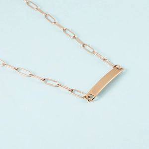Macro view of rose gold paperclip chain and polished rectangular pendant on blue background