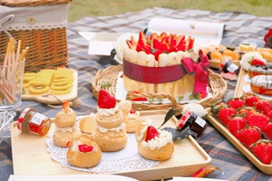 Close-up of strawberry cakes and puff pastries in a woven picnic basket on green grass