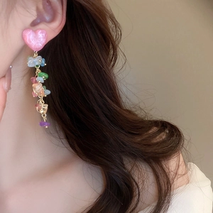 Détail de boucles d'oreilles cœur rose avec pampilles en pierres colorées sur modèle