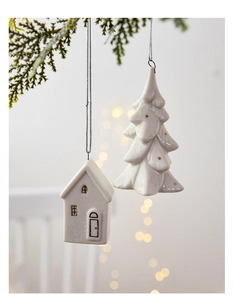 Hanging white ceramic house and Christmas tree decorations on evergreen branches