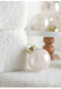 Detail of elegant champagne Christmas balls with feathers inside on a white texture