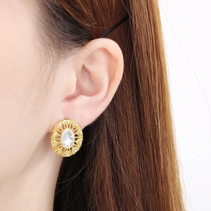 Close-up of gold-plated textured round stud earring with pearl and crystal on ear