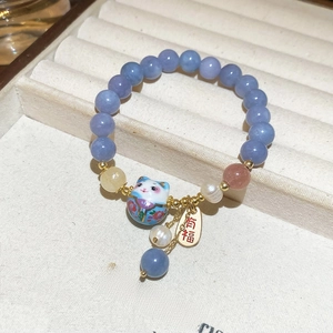 Dettaglio bracciale di perle con ciondolo gatto portafortuna e targhetta dorata