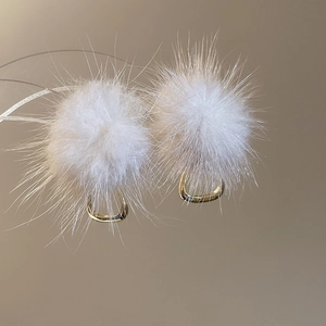 Close-up of white plush pom-pom earrings with golden U-shaped metal clips for women