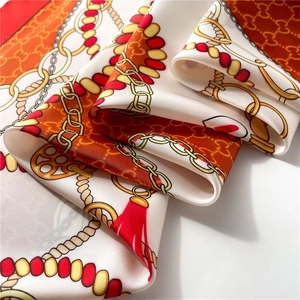 Macro detail of luxury silk scarf showing chain print and tassel pattern on fabric