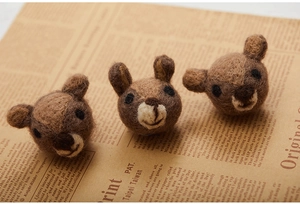 Close-up of handmade wool felt animal charms in brown and beige on vintage newspaper