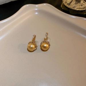 Close-up of elegant gold pearl earrings with zircon inlay on a beige display tray