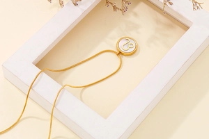 Detailed shot of gold Leo zodiac necklace with white shell pendant on beige background