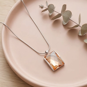 Detail of champagne crystal pendant on a silver snake chain over ceramic tray
