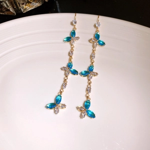 Détail de boucles d'oreilles dorées à pompons avec pierres bleues sur assiette blanche
