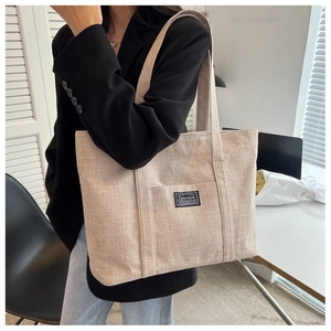 Shoulder view of a beige canvas tote bag with fashion label and large capacity design