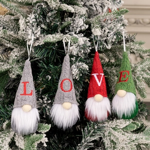 Close-up of knitted Christmas gnomes with L-O-V-E embroidery hanging on a snowy tree