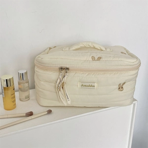 Detailed close-up of rabbit embroidery on a beige quilted cosmetic bag with dual zippers