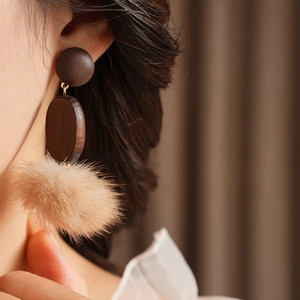 Close-up of stylish retro earrings with round wood studs and beige pom-poms on ear