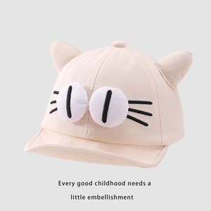 Detail of baby baseball cap with 3D cat ears and large embroidered eyes on soft beige canvas