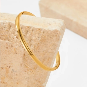 Primer plano de un brazalete ovalado de acero inoxidable dorado pulido en piedra.
