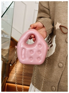 Detail of pink jelly PVC handbag with round dimple design and gold chain strap held by hand