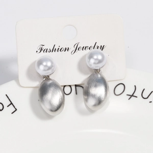 Detailed view of brushed silver oval earrings with white pearls on jewelry card