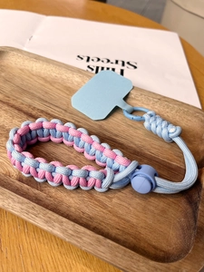 Detail of pink and blue woven phone wrist strap with adjustable buckle on wooden tray