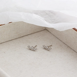 Macro detail of silver bubble stud earrings with cubic zirconia on beige linen