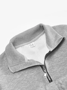 Detail shot of the zipper collar and fabric label on a grey quarter-zip knitted sweater