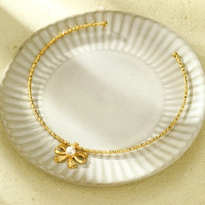 Elegant gold bowknot necklace with a central pearl pendant on a textured round tray