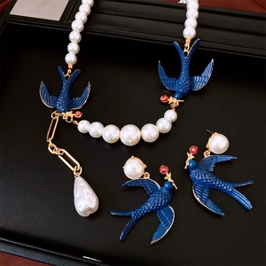 Macro detail of bird pearl necklace and earring set with blue swallow and red flower motifs