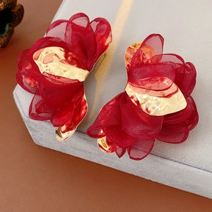 Detail of red chiffon flower earrings with textured gold metal center on velvet stand