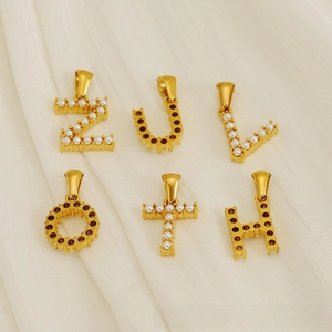 Détails des pendentifs lettres dorées sertis de zircons sur velours beige doux