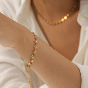 Gold-plated stainless steel bracelet with blue flower enamel charms on a female wrist