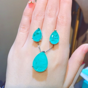 Detailed view of pear-cut emerald earrings and pendant set on hand for size reference