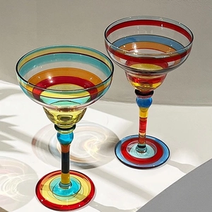 Hand-painted colorful striped margarita glass set on white surface with vivid light shadows