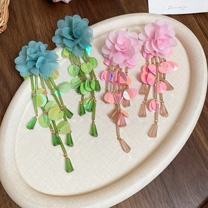 Detail of long floral chiffon tassel earrings in green and pink on a wooden tray