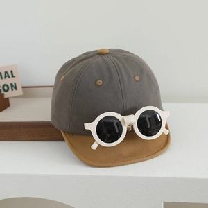 Détail d'une casquette bébé avec lunettes de soleil intégrées sur une surface blanche pure