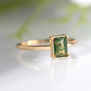 Close-up of elegant gold ring with rectangular green gemstone and four-prong setting