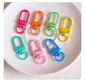Macro shot of 7 colorful alloy lobster clasps with rotating rings in a white ceramic dish