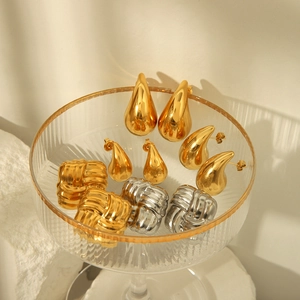 Boucles d'oreilles gouttes dorées 18k et puces nœuds texturées sur un plateau en verre