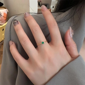 Detail of a thin gold rope ring with a single green gemstone worn on a hand