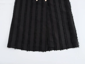 Détail de robe noire avec boutons dorés et texture de franges verticales effilochées