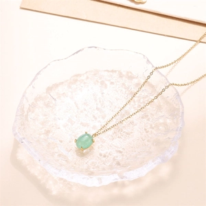 Detailed shot of a green oval gemstone pendant on a gold chain in a textured glass bowl