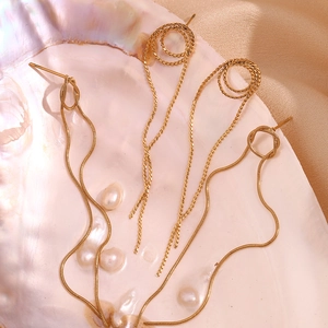 Macro view of gold snake chain long tassel earrings with intricate knot design on a shell