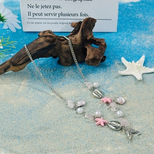 Close-up of ocean-themed beaded necklace with pink starfish and shell charms on beach sand