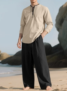 Close-up of beige linen Henley shirt and black drawstring pants for men on a beach
