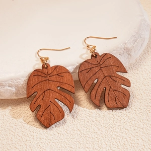 Detailed view of monstera leaf wooden earrings with golden hooks on stone background