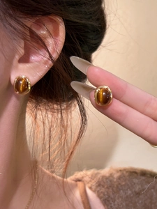 Detailed view of oval tiger eye stud earrings with 18k gold plating on a model