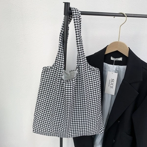 Detail of classic black and white gingham canvas tote bag hanging with stylish black blazer