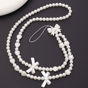 Detail of white pearl phone lanyard with elegant bow and seashell charms on black background