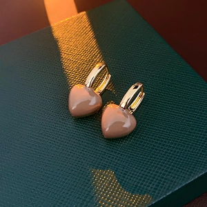 Macro view of gold heart earrings on dark green leather, showing glossy enamel detail