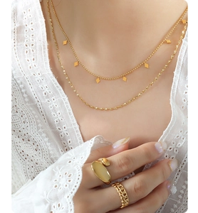 Dettaglio della collana dorata a due strati e degli anelli indossati con pizzo bianco